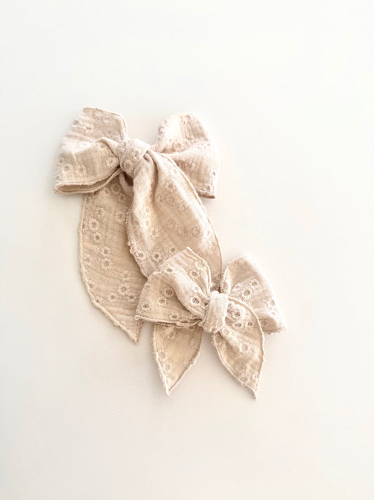Neutral embroidered linen bow in petite and midi sizes on alligator clip and nylon headband.