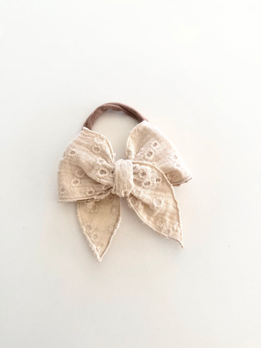 Neutral embroidered linen bow in petite and midi sizes onalligator clip and nylon headband.